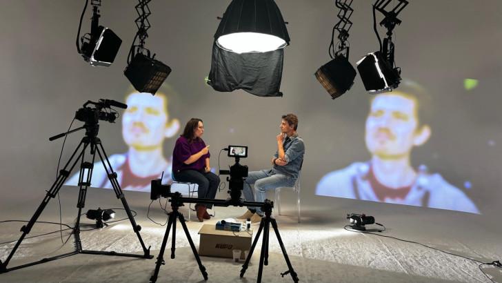 Plateau de l'émission, au premier plan des caméras. On aperçoit les projecteurs et deux invités discutant. Au fond, le portrait de François Giraud